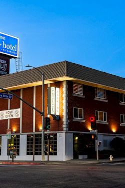 A street view of a brick hotel with bright signage and palm trees under a clear blue sky.