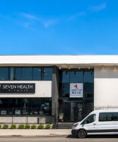 A storefront clinic building with signs for Seven Health Fitness and Urgent Care, under a clear blue sky.